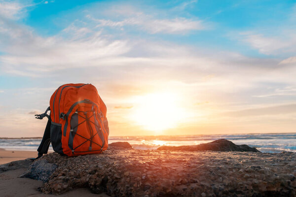 Апельсиновый рюкзак на берегу моря в фантастическую погоду. Концепция страхования путешествий. Путевой свет