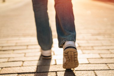 Genç kız öğrencinin bacakları eğleniyor ve gün batımında şehirde asfalt bir sokakta yürüyor.