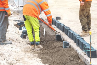 İnşaat alanındaki beton kaldırımları kürekle döşeyen yer işçileri yüksek-Viz 'de