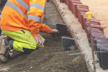 Groundworker in hi-viz leveling semi-dry concrete and kerbs on new road construction clipart