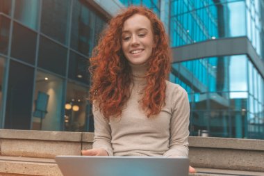 İş merkezinin önünde dizüstü bilgisayar kullanan gülümseyen bayan.