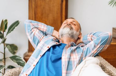 Oturma odasındaki kanepede oturan yaşlı, mutlu yaşlı bir adam.