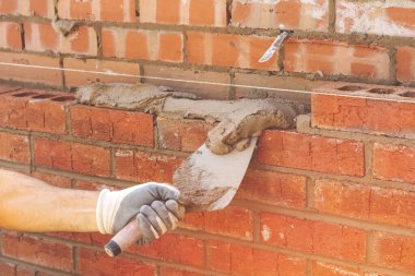 İnşaat alanında tuğla döşeyen koruyucu eldivenli Masonry Trowel ile tuğla ustası.