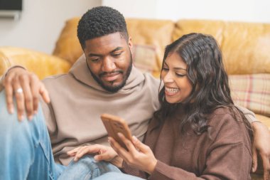 Kanepede oturan çift akıllı telefon kullanarak sarılıyor. Gerçek insan yaşam tarzı.