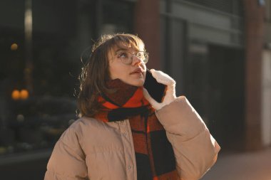 hevesli genç kız öğrenci gün batımında telefonla şehirde dolaşıyor.