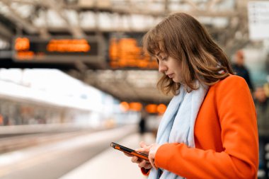 Platformdaki tren istasyonunda telefonu kullanan genç bir kadın gezgin.
