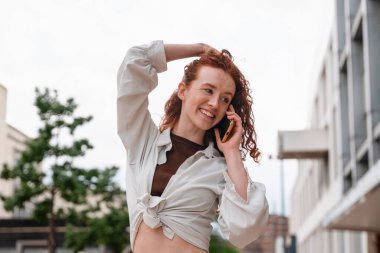 Sokak yaşam tarzı konseptinde telefon kullanan kızıl saçlı genç bir kadın.