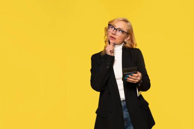 Elleri yanaklarında olan kadın, hesap makinesini fotokopi alanı olan sarı arka planda tutmayı düşünüyor.