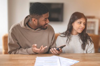 Bir çift masada oturmuş, mali konuları ciddi bir ifadeyle tartışıyorlar. Konforlu bir evde finansal tartışma anı