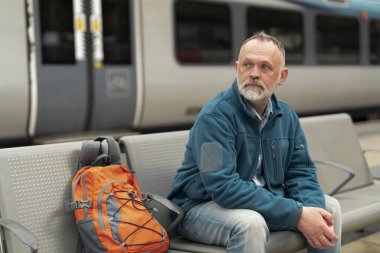 Sırt çantalı bir adam treni bekliyor. 