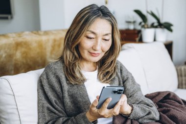 Oturma odasında akıllı telefon kullanan kadın.