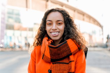 Şehrin caddesinde Turuncu Ceket ve Atkı Giyen Gülümseyen Kadın