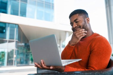 Modern binanın dışında dizüstü bilgisayar kullanırken Adam Gülümsüyor