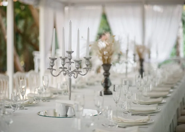 Soft-focus chandelier on white tablecloth. Table setting for many person on background of white curtains. Side-view angle.
