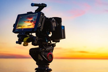 Profesyonel kamera tripodun üzerinde gün batımının görüntülerini çekiyor..