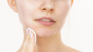 Yüzünde maske olan genç bir kadın pamuklu bezle kozmetiği temizliyor. Cildiyle ilgilenen genç bir kız. Güzellik tedavisi. Cilt bakımı.