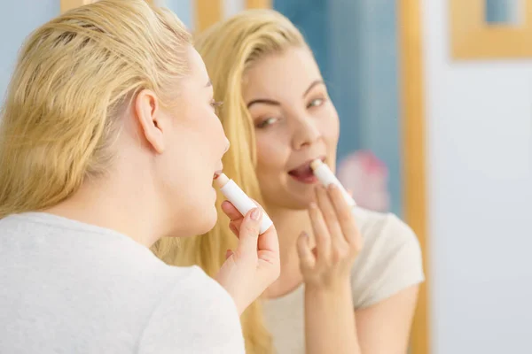 在浴室里的金发妇女应用唇膏保湿香脂 照顾她的嘴唇皮肤 — 图库照片