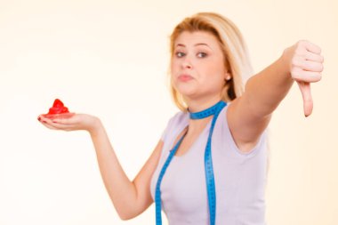 Şekerleme, abur cubur, şeker günaha diyet kavramı. Teyp başparmak aşağı jest gösterilen tatlı çilek cupcake tutarak onun boynuna ölçme ile kadın.