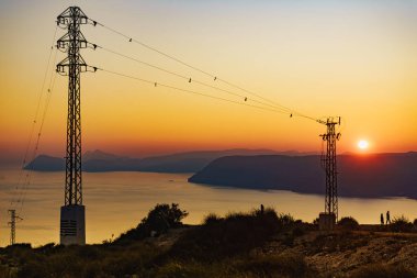 Elektrik iletim direkleriyle kıyı şeridi, elektrik hatları yüksek voltaj kuleleri. İspanya 'da günbatımı manzarası