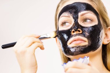 Yüzüne siyah detoks çamur maskesi süren genç bir kadın. Deriyle ilgilenen bir kız. Güzellik tedavisi. Cilt bakımı.