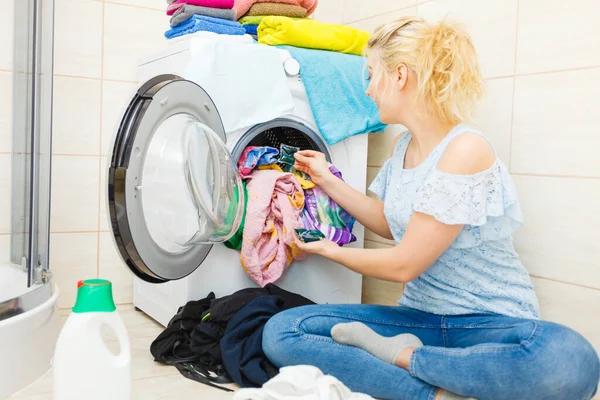 Woman in bathroom sorting different colored clothes laundry for washing in machine, using detergent pods gel capsules. Household duties chemicals objects.