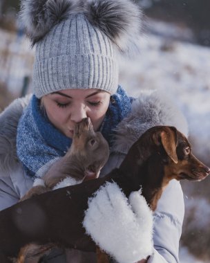 Genç bir kadın dışarıda karda eğleniyor. Dişi, soğuk kış gününde küçük safkan köpekleriyle oynuyor..