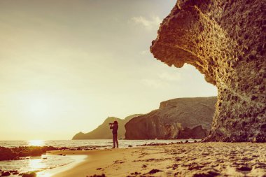 Kameralı turist kadın gün batımında Monsul sahilinde fotoğraf çekiyor. Cabo de Gata Nijar Doğal Parkı, Almerya, Endülüs, İspanya.