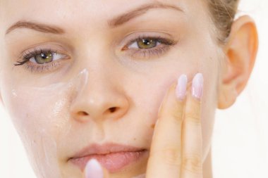 Genç bir kadın krem kozmetik uyguluyor, yüzüne nemlendirici maske takıyor. Güzellik tedavisi. Cilt bakımı.