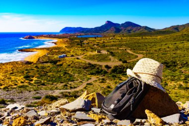 Şapka ve sırt çantası, Akdeniz kıyısında yaz yürüyüşü ekipmanları. Murcia bölgesi, Calblanque Bölgesel Parkı, İspanya. Yürüyüş, kamp, aktif yaşam tarzı.