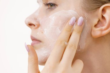 Genç bir kadın krem kozmetik uyguluyor, yüzüne nemlendirici maske takıyor. Güzellik tedavisi. Cilt bakımı.