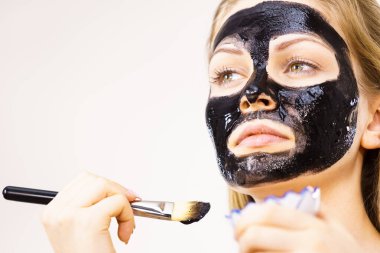 Yüzüne siyah detoks çamur maskesi süren genç bir kadın. Deriyle ilgilenen bir kız. Güzellik tedavisi. Cilt bakımı.