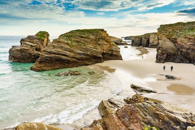 People walking on Cathedrals Beach at low tide, Playa las Catedrales in Ribadeo, province of Lugo, Galicia. Cantabric coast in northern Spain. Tourist place. clipart