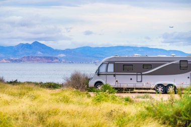 Caravan on mediterranean coast, Alicante city in the distance, Costa Blanca Spain. Wild camping on beach. Vacation trip with motor home.