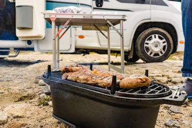 Et ve sosis ızgarada. Barbekü yemeği, yaz yemeği. Arka planda karavan vagonu var..