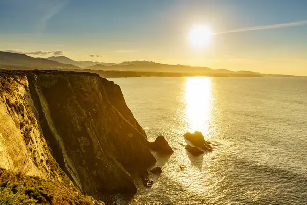 Kuzey İspanya 'daki Asturias kıyısındaki kayalık kayalıkların üzerinde gün batımı. Faro de Cabo Busto 'dan görüntü. Turistik yerler, ziyaret edilecek yerler..