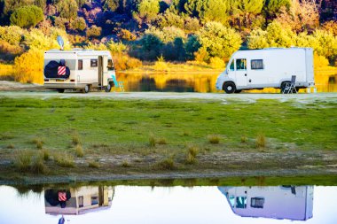 Camping on nature. Camper vehicles at lake shore reflecting in water. Povoa e Meadas Dam in Castelo de Vide, Alentejo Portugal. Travel in motor home. clipart