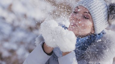 Genç ve güzel kadın onunla oynamak kar üfleme. Erkek çiçekler ve eşarp mavi gri bere sıcak şapka sahip.