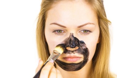 Genç bir kadın yüzünde siyah detoks çamuruyla fırça kömür maskesi takıyor. Yağlı ciltle ilgilenen bir kız. Güzellik tedavisi. Cilt bakımı.