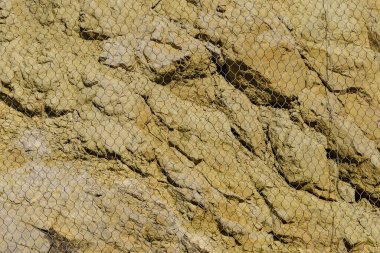 Grunge duvar taşı ya da sert doğa kayası. Dağdan ya da kayalıklardan kayarak kayan kayalardan korunmak için ağlı..