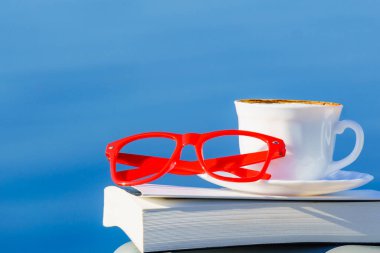 Tatilde okumak. Kahve fincanı, kitap ve kırmızı bardaklar mavi deniz suyuna karşı. Tatil gezisinde dinlenmek. Zihinsel sağlık sorunları.