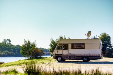 Karavan göl kıyısında kamp yapıyor. Kamp aracının çatısında uydu anteni. Televizyon bağlantısı. Tatillerde karavanda seyahat..