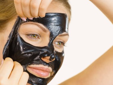 Young woman removing carbo black peel-off mask from her face, on white. Teen girl taking care of oily skin, cleaning the pores. Beauty treatment. Skincare. clipart