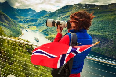 Tourism holidays picture and traveling. Woman tourist enjoying fjord landscape Geirangerfjord from Ornesvingen eagle road viewpoint, taking photo with camera, Norway. clipart