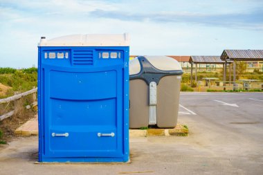 Taşınabilir tuvalet ve sanayi tipi çöp tenekesi park alanında.