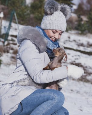 Genç bir kadın dışarıda karda eğleniyor. Dişi, soğuk kış gününde safkan köpek yavrusuyla oynuyor..