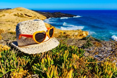 Summer hat and sunglasses on mediterranean sea coast. Murcia region, Calblanque Regional Park in Spain. Hiking, camping, active lifestyle. clipart