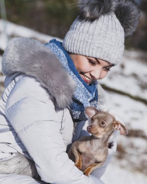 Genç bir kadın dışarıda karda eğleniyor. Dişi, soğuk kış gününde safkan köpek yavrusuyla oynuyor..