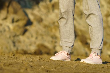 Kumsalda yürüyen, dinlenen bir kadın. Spor ayakkabılarla bacakları detaylandır. Yaz tatili.
