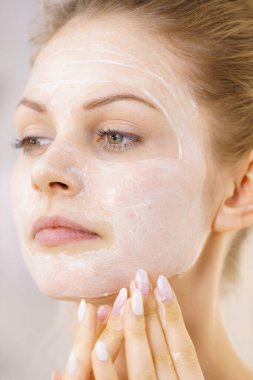 Genç bir kadın krem kozmetik uyguluyor, yüzüne nemlendirici maske takıyor. Güzellik tedavisi. Cilt bakımı.