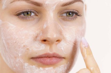 Genç bir kadın krem kozmetik uyguluyor, yüzüne nemlendirici maske takıyor. Güzellik tedavisi. Cilt bakımı.